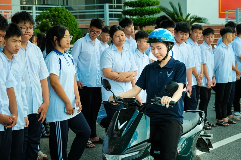 Nhân viên Tiến Cảnh đội mũ xanh, hướng dẫn bên xe VinFast trước nhóm học sinh.