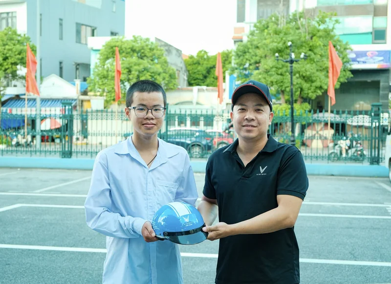 Nhân viên Tiến Cảnh và học sinh cùng cầm mũ bảo hiểm mang tên VinFast Tiến Cảnh.